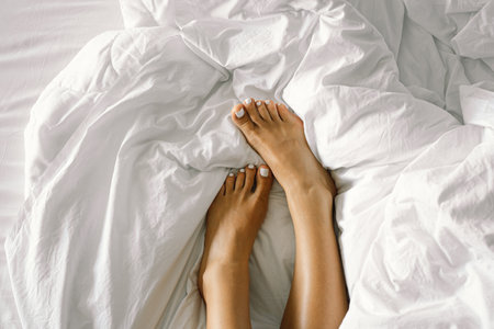 Female feet with a white pedicure on a white bed in the bedroom. Foot care, pedicure. Spa body careの写真素材