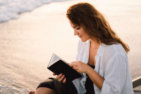 Christian woman holds bible in her hands. Reading the Holy Bible on the sea during beautiful sunsetの写真素材