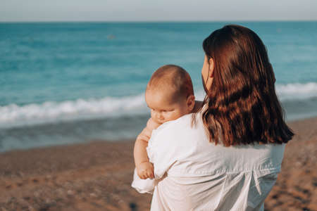 A young mother walks along the beach with a small child in diapers.の写真素材