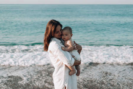 A young mother walks along the beach with a small child in diapers.の写真素材