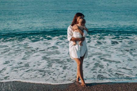 A young mother walks along the beach with a small child in diapers.の写真素材