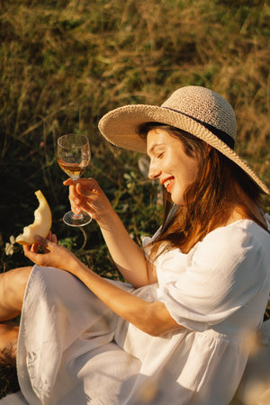 Young beautiful girl in a white dress having a picnic with a glass of champagne or white wineの写真素材