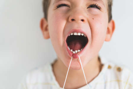 Cute boy pulling loose tooth using a dental floss. Process of removing a baby tooth.の写真素材