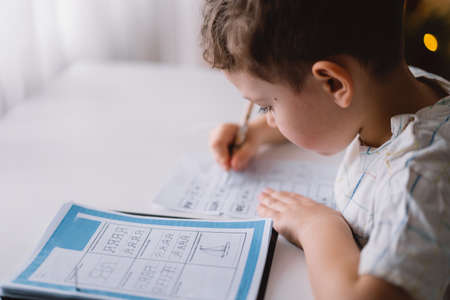 Cute kid boy studying at home and doing school homework. Thinking child sitting at table.の写真素材