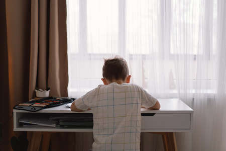 Cute kid boy studying at home and doing school homework. Thinking child sitting at table.の写真素材