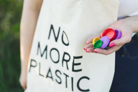 Woman hands are holding a handful of multi-colored plastic lids. Concept of environmental pollution