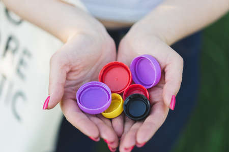 Woman hands are holding a handful of multi-colored plastic lids. Concept of environmental pollution