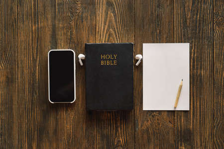 Church online Sunday new normal concept. Bible, cell phone and earbuds on a wood background.