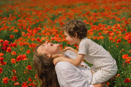 Happy Mothers Day. Little boy and mother is playing in a beautiful field of red poppiesの写真素材
