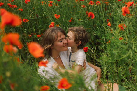 Happy Mothers Day. Little boy and mother is playing in a beautiful field of red poppiesの写真素材