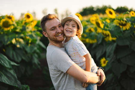 Father with little baby son in sunflowers field during golden hour. Dad and son are active in nature.の写真素材