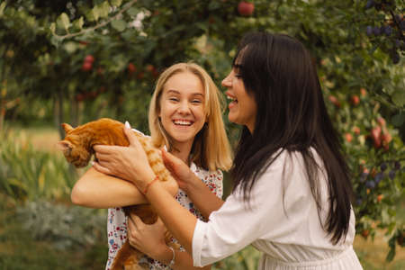 A young mother with a teenage daughter playing with a ginger cat in the garden.