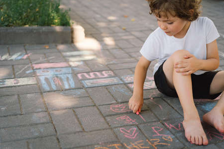 little preschool boy draws with colorful chalks on the ground.の写真素材