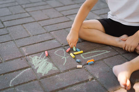 little preschool boy draws with colorful chalks on the ground.の写真素材