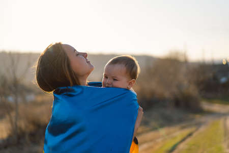 Woman hugs her little son wrapped in yellow and blue flag of Ukraine in outdoors.の写真素材