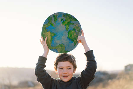 Little boy holding planet in hands against green spring background. Earth day