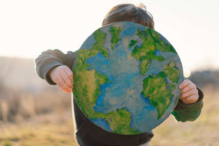 Little boy holding planet in hands against green spring background. Earth day