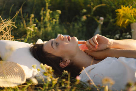 Beautiful romantic young woman lying on a blanket on a summer meadow. Time for yourself.の写真素材