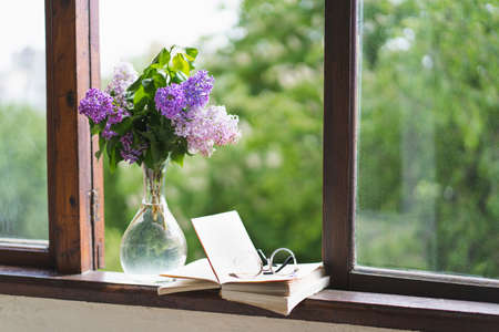 Book, glasses and lilac on a wooden window.