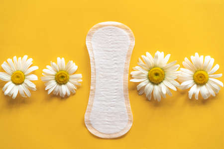 Menstruation period concept. Hygienic white female pad with chamomile flowers on yellow background