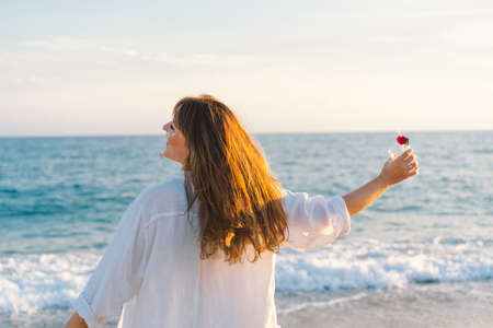 Portrait of a young girl in a straw hat with a cocktail in hand on a background of beautiful seaの写真素材