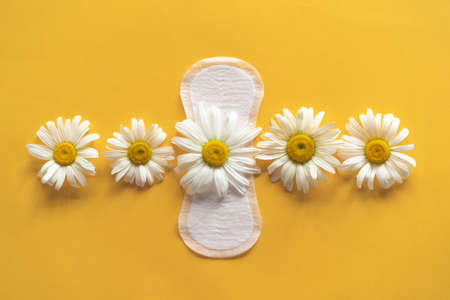 Menstruation period concept. Hygienic white female pad with chamomile flowers on yellow backgroundの写真素材