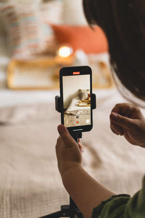 A young woman is filming home goods for her online store on her phone camera.