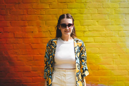 Portrait of happy smiling young woman with sunglass on colorful orange backgroundの写真素材