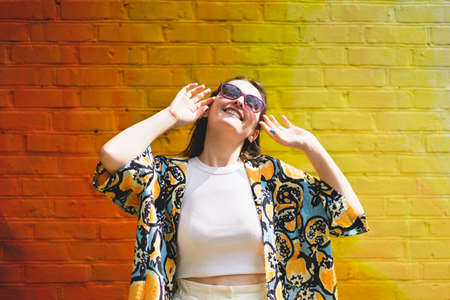 Portrait of happy smiling young woman with sunglass on colorful orange backgroundの写真素材