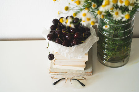 Book, cherries and vase with chamomile flowers. Read and rest. Cozy spring concept.