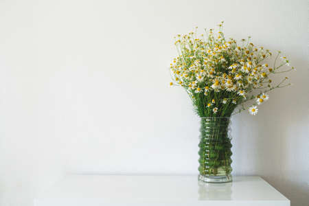 a bouquet of daisies in a white glass vase on a white tableの写真素材