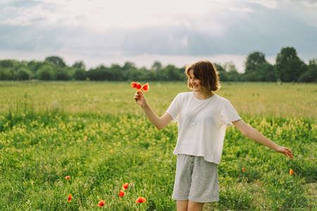Happy Cheerful Teen Girl With Pronounced Face dancing In Outdoors in a field with red poppies.の写真素材
