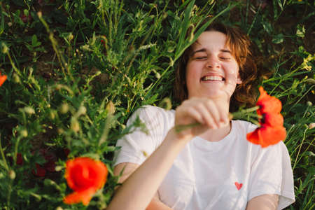 Happy Cheerful Teen Girl With Pronounced Face dancing In Outdoors in a field with red poppies.の写真素材