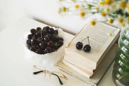Book, cherries and vase with chamomile flowers. Read and rest. Cozy spring concept.の写真素材