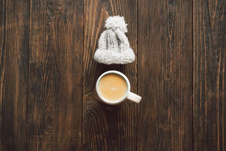 Cup of coffee and autumn dried leaves, knitted little hat on wood background. Flat layの写真素材