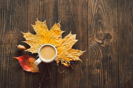 Cup of coffee and autumn dried leaves on wood background. Flat lay