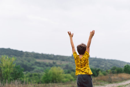 A six-year-old boy is standing with his back in the countryside. Back view.