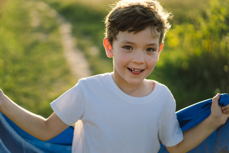 Ukrainian child boy in white t shirt with yellow and blue flag of Ukraine in field.の写真素材