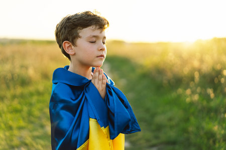 Ukrainian boy closed her eyes and praying to stop the war in Ukraine in a field at sunsetの写真素材
