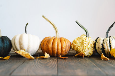 Multicolored pumpkins and dry autumn leaves on wooden background.の写真素材
