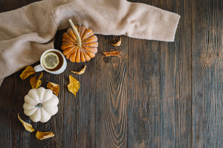 Flat lay of pumpkins, dried leaves, accessories and tea with lemon in cup on wooden background.の写真素材