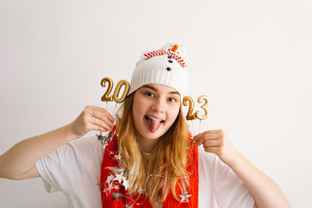 Funny young girl in a New Years hat and red scarf holds the numbers 2023 in her hands.の写真素材
