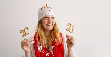 Funny young girl in a New Years hat and red scarf holds the numbers 2023 in her hands.の写真素材