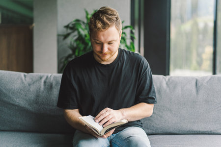 Beauty young man is reading a book at home. Thoughtful man reading important book.の写真素材