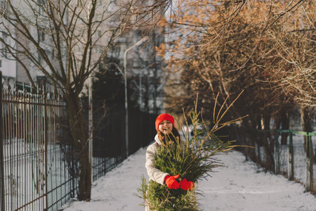 A beautiful girl in a red hat carries a Christmas tree.の写真素材