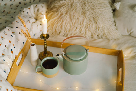 Cup of tea and teapot on a serving tray on a bed.