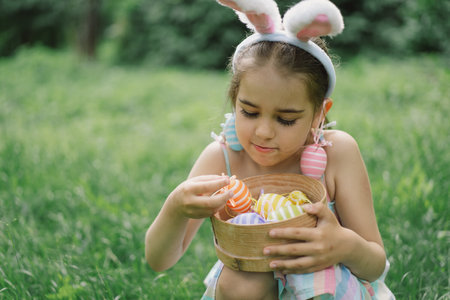 Girl with eggs basket and bunny ears on Easter egg hunt in garden.