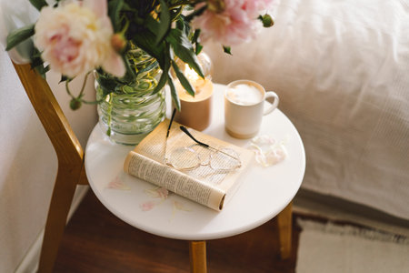 Open book with glasses, cup coffee and bouquet white pink peonies flowers. Read and rest. Cozy home