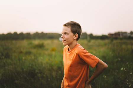 Portrait of a smiling little boy in a orange T-shirt and playing outdoors on the field at sunsetの写真素材
