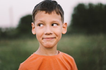Portrait of a smiling little boy in a orange T-shirt and playing outdoors on the field at sunsetの写真素材
